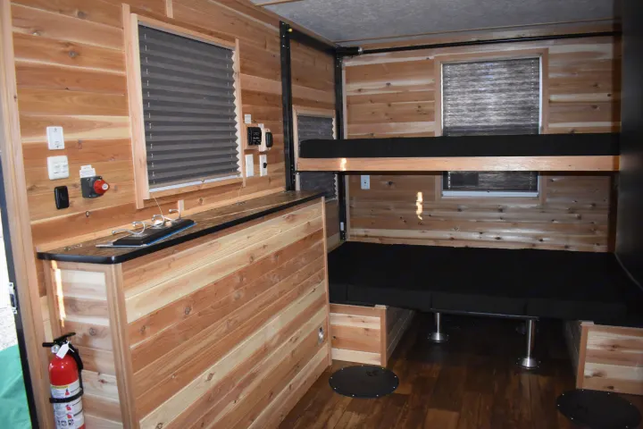 Cozy rv rental interior featuring rustic wood paneling, comfortable bunk beds, and floor openings for ice fishing.. Ice Castle Fish Houses Rv Edition Standard 2024
