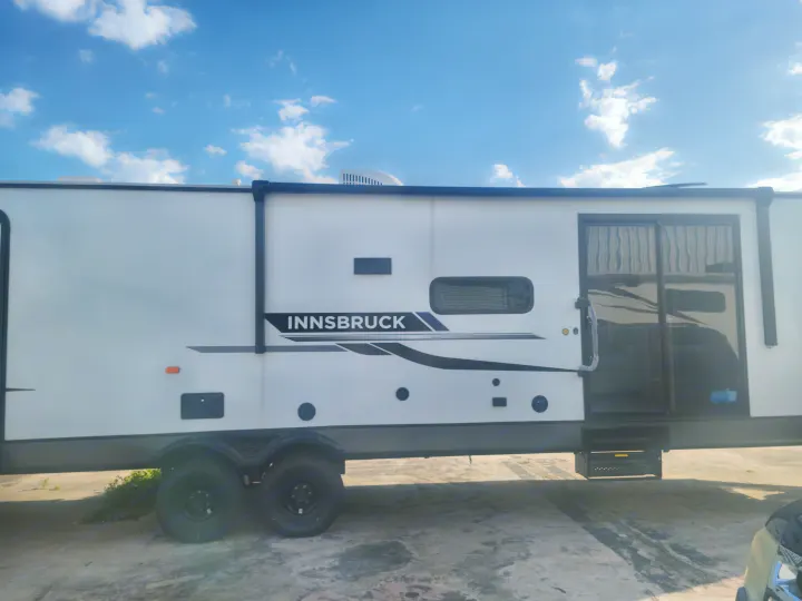 Side view of a white Innsbruck RV for rental, featuring a large door & multiple windows under a clear sky.. Gulf Stream Innsbruck 2023