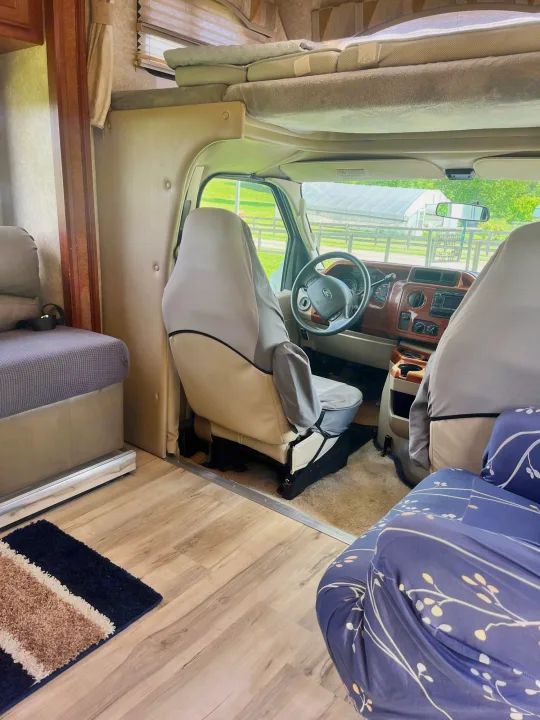 Experience RV rental comfort: spacious interior looking into the cockpit with a bunk above and scenic views outside.. Ford Fourwinds 2009