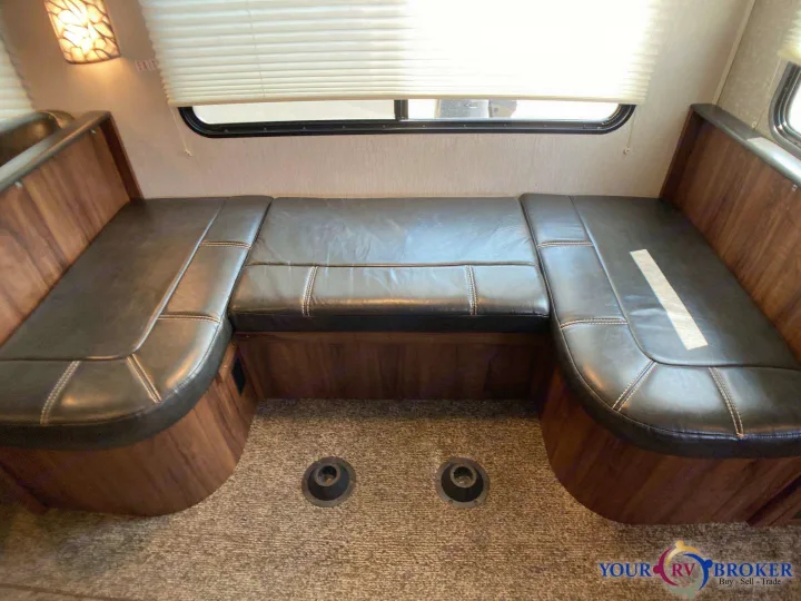 Inside an RV rental: Cozy dinette area with dark brown leatherette booth seating, wooden base, and window with blinds.. Heartland RVs Mallard 2019