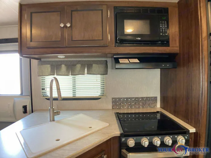 Inside an RV rental kitchen featuring a compact sink, stovetop, microwave, and overhead cabinets for convenient travel cooking.. Heartland RVs Mallard 2019