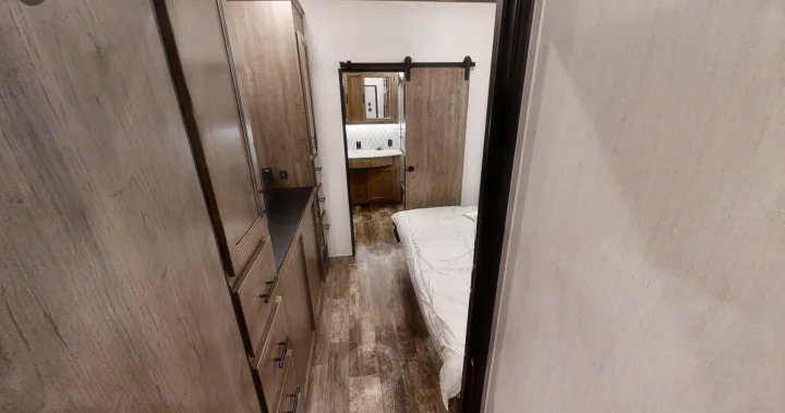 Cozy RV rental bedroom and bath. Features a modern interior with wooden cabinets, a bed, and a bathroom with a barn door.. Forest River Sabre 2022
