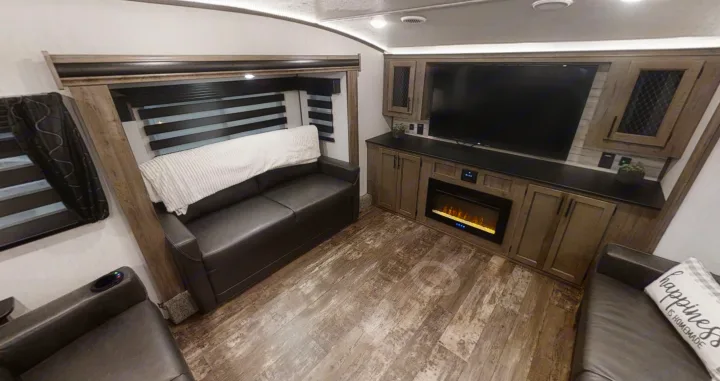 Spacious RV rental living area with a dark sofa, large TV, electric fireplace, and modern wood-look flooring.. Forest River Sabre 2022