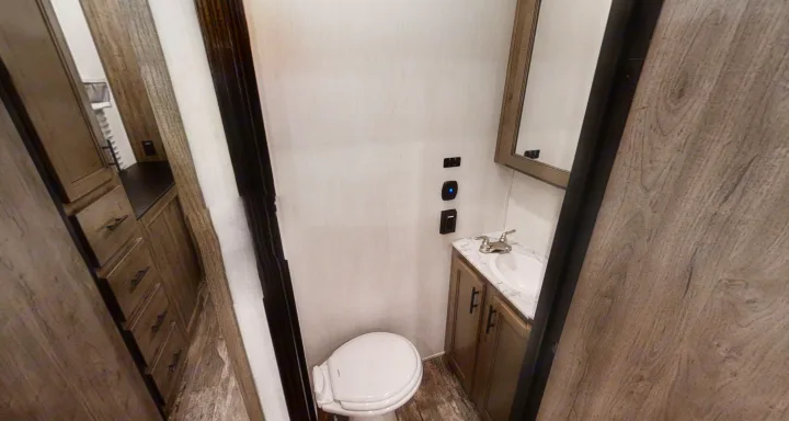 Step into this RV rental's compact bathroom with a white toilet, sink vanity, and wood-look cabinetry. Wall-mounted controls are visible.. Forest River Sabre 2022