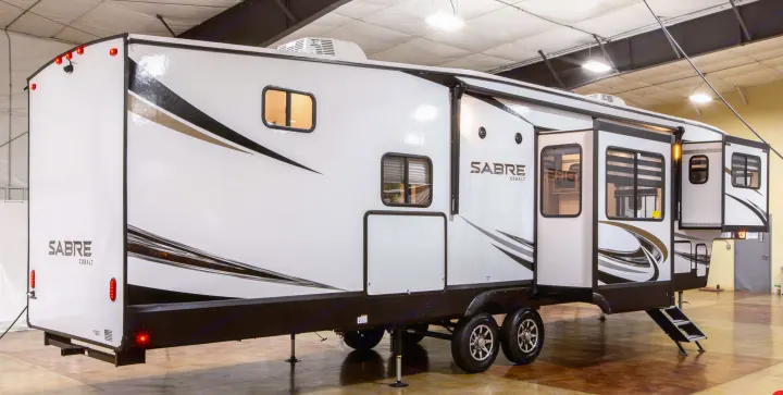 Spacious white fifth-wheel RV rental with black & gold graphics, multiple windows, and extended slide-outs shown indoors.. Forest River Sabre 2022