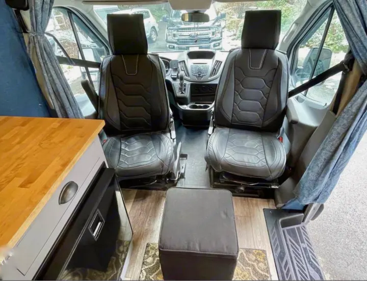 RV rental: Camper van interior showing swivel front seats, a compact kitchen counter on the left, and a central ottoman.. Ford Transit 2019