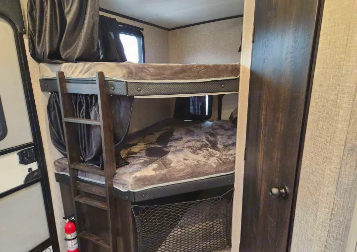 Bunk beds in an RV rental offer a compact sleeping area. Features include a ladder, curtains, and a visible fire extinguisher.. Jayco Whitehawk 2023