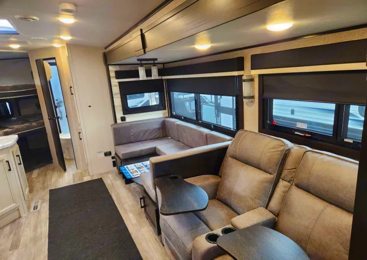 Spacious rv rental interior showing living area with recliners, L-sofa, bunk beds, and bathroom access.. Jayco Whitehawk 2023