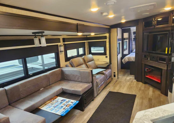 Spacious RV rental living area featuring a large sofa, recliners, entertainment center with fireplace, and connected bedroom.. Jayco Whitehawk 2023