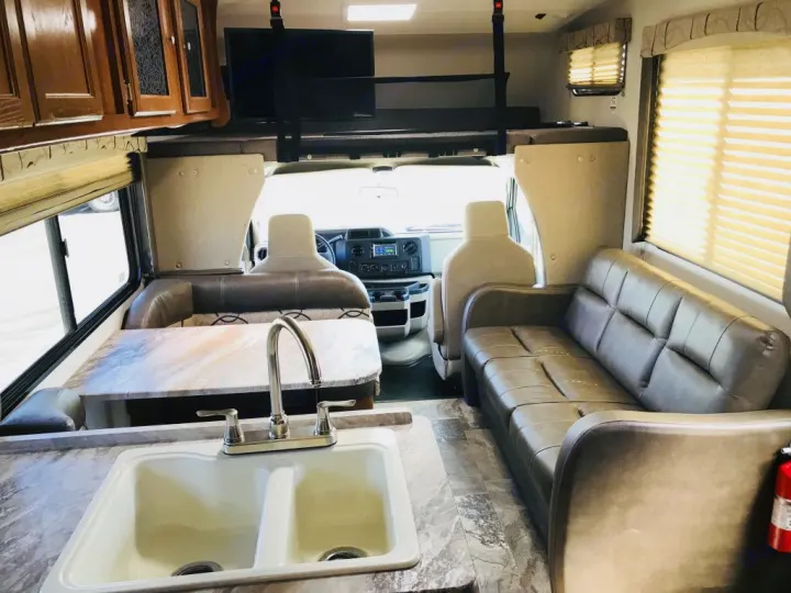 RV rental interior features a dinette, kitchen sink, comfy sofa, and overhead bunk bed with TV. Perfect for road trips!. Coachmen Leprechaun 2016