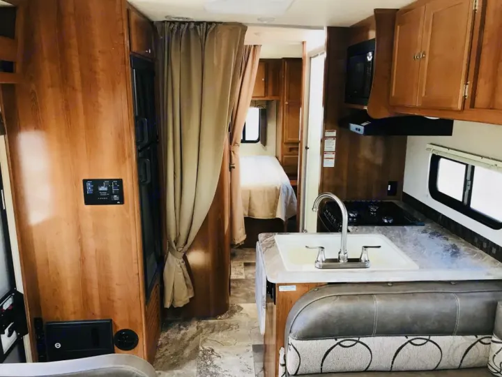 Inside this RV rental: wood-toned interior with kitchen (sink, stove, microwave), dinette, fridge, & curtained bedroom.. Coachmen Leprechaun 2016