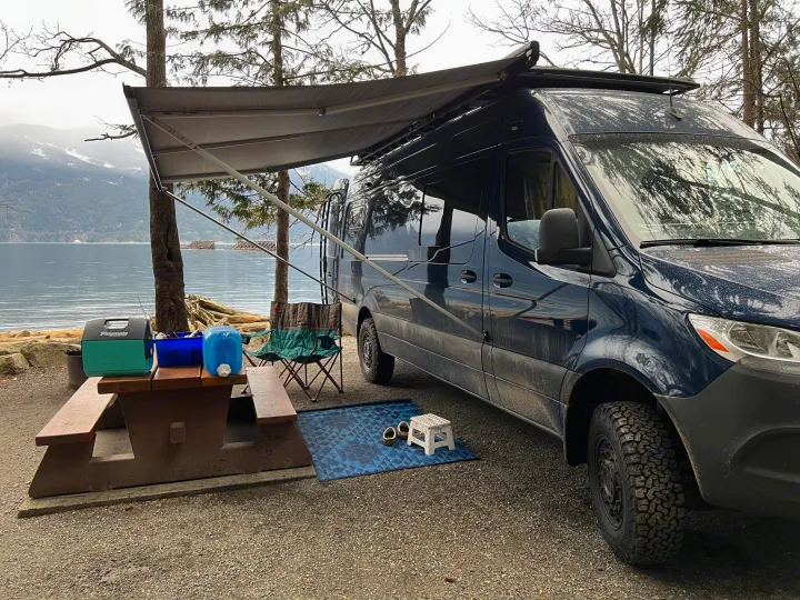 Waterfront rv rental camping with a blue van, picnic table, & awning setup, offering views of the lake & mountains.. Mercedes Sprinter 2022
