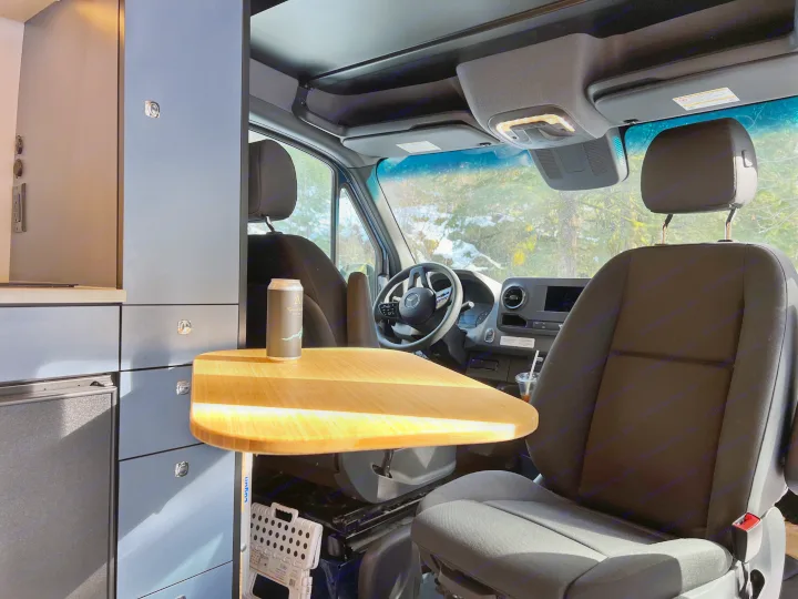 Spacious RV rental camper van interior. Features front seats, wood table, cabinetry, and snowy scenery outside.. Mercedes Sprinter 2022