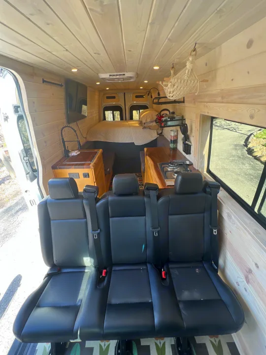 Spacious RV rental interior featuring wood paneling, a comfy bed, kitchen area, and three passenger seats.. Mercedes-Benz Sprinter RV Motorhome Campervan 2022
