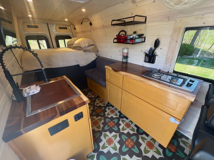 Inside this bright rv rental: wood-paneled walls, bed, kitchen with stove and sink, and a cozy dining bench.. Mercedes-Benz Sprinter RV Motorhome Campervan 2022