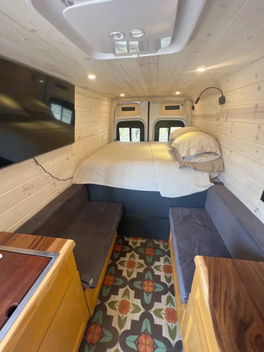 View inside an rv rental: Wood-paneled walls & ceiling, full bed at back, colorful tiled floor, and side bench seating with a kitchenette.. Mercedes-Benz Sprinter RV Motorhome Campervan 2022