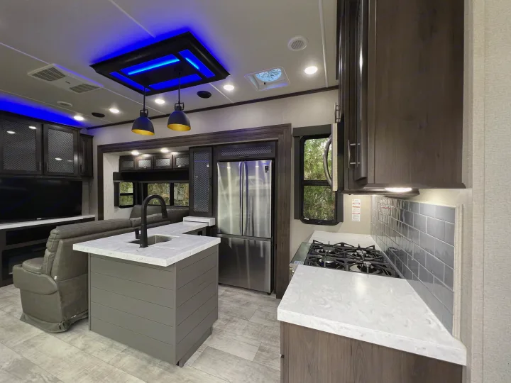 Modern RV rental interior with a spacious kitchen island, stainless steel appliances, and ambient blue lighting.. Grand Design Momentum Toy Hauler 2022