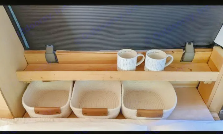 RV rental storage: Wooden shelf with mugs, three rope baskets, and a dark blind inside a custom camper interior.. Chevrolet Other 1996