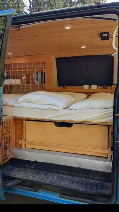 RV rental: A cozy, wooden-paneled camper van interior featuring a comfy bed, pull-out storage, and a built-in bookshelf.. Chevrolet Other 1996