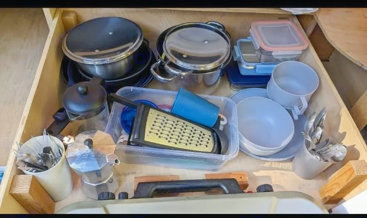 RV rental kitchen drawer neatly packed with pots, pans, bowls, cups, grater, cutlery, and coffee makers for travel meals.. Chevrolet Other 1996