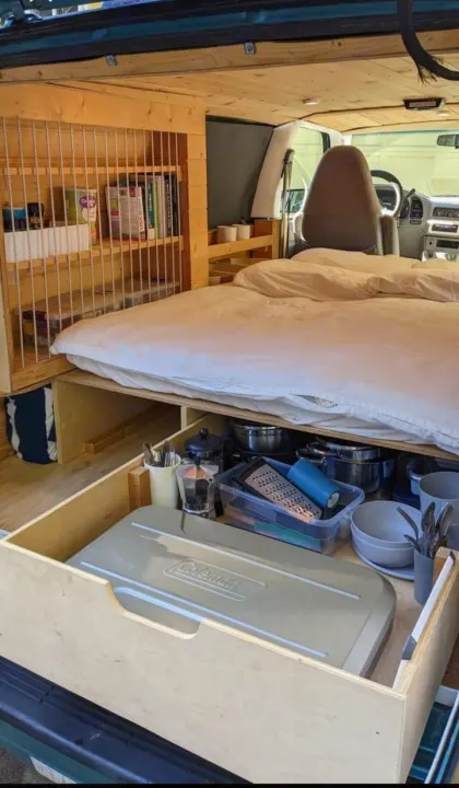 Inside a well-organized RV rental camper van: a comfy bed, custom shelving, and a pull-out kitchen with stove.. Chevrolet Other 1996
