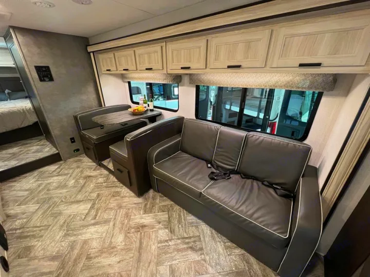 Step into this modern RV rental's living space: dark gray sofa, dinette, and a glimpse of the bedroom.. Forester LE 2022