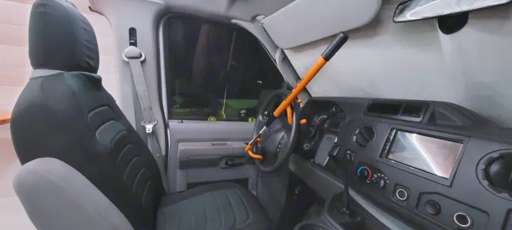 Inside a secure rv rental: Driver's seat, dashboard, and orange Club anti-theft device on the steering wheel.. Ford E250 2009