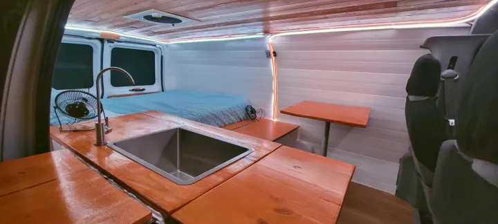Cozy RV rental interior showcasing a camper van conversion with kitchen sink, bed, table, and ambient lighting.. Ford E250 2009