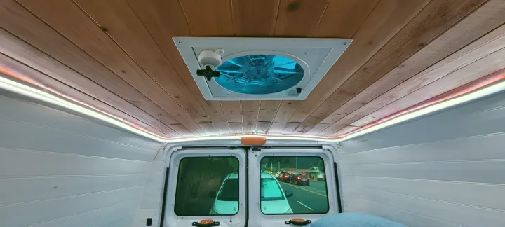 Inside a customized RV rental: wood plank ceiling, bright blue fan, ambient LED lighting, and a view of traffic through rear windows.. Ford E250 2009