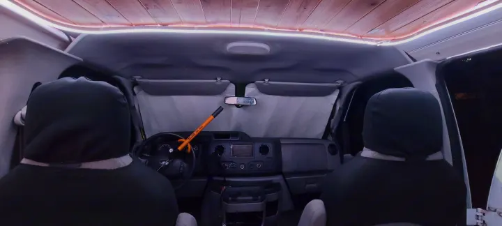 RV rental van interior at night, showing dashboard, steering wheel with anti-theft bar, and custom LED wood ceiling.. Ford E250 2009