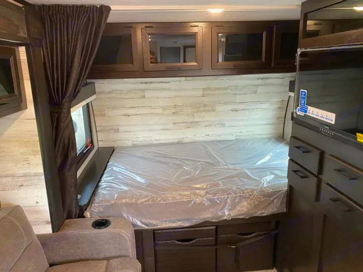 RV rental interior: Clean bedroom area with plastic-covered bed, wall-mounted TV, and dark wood storage cabinets.. Jayco 166 FBS 2022
