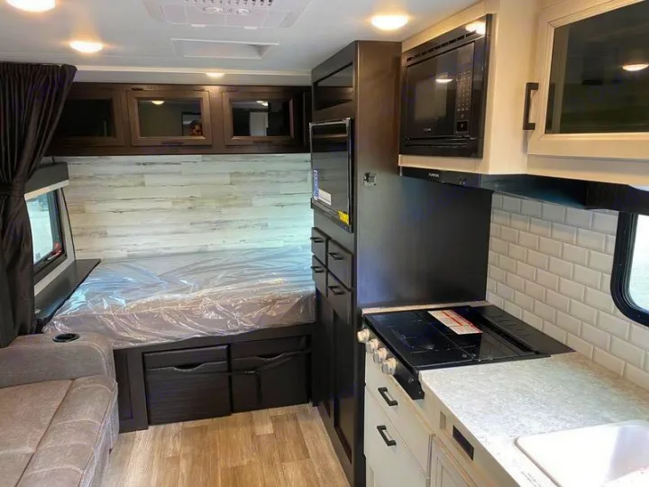 Inside an RV rental: a compact living space featuring a comfortable bed, functional kitchen with stove and microwave, plus storage.. Jayco 166 FBS 2022