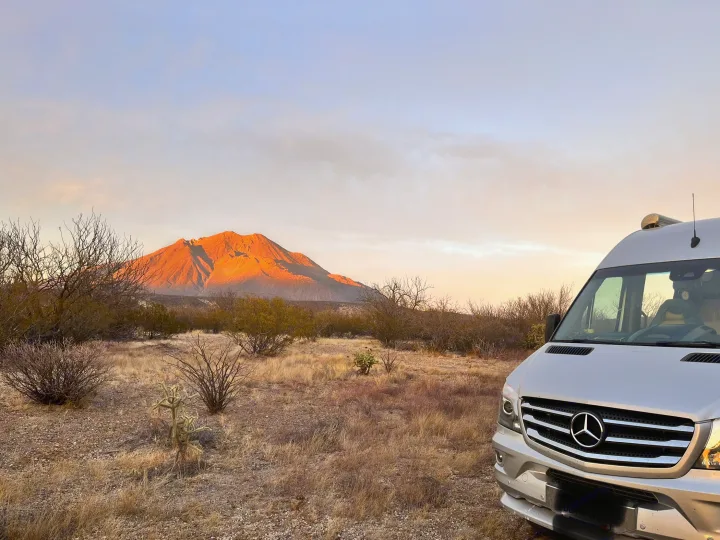 A silver RV rental parked in a desert landscape with a mountain glowing orange under a beautiful sunset sky.. Airstream Interstate 2017