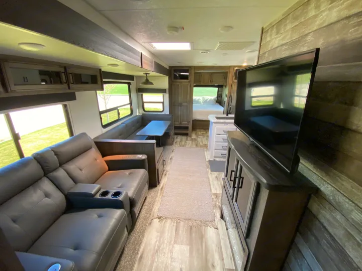 Spacious and modern RV rental interior featuring a living area with recliners, dining booth, kitchen, and cozy bedroom.. Venture Sporttrek 2022