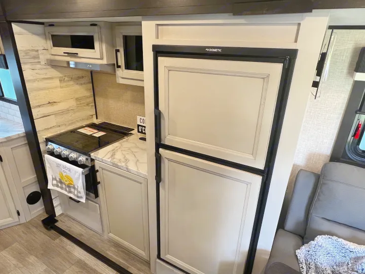 RV rental kitchen interior: a Dometic refrigerator, stovetop, and light wood-look cabinets offer comfort on your road trip.. Jayco 21MML 2023