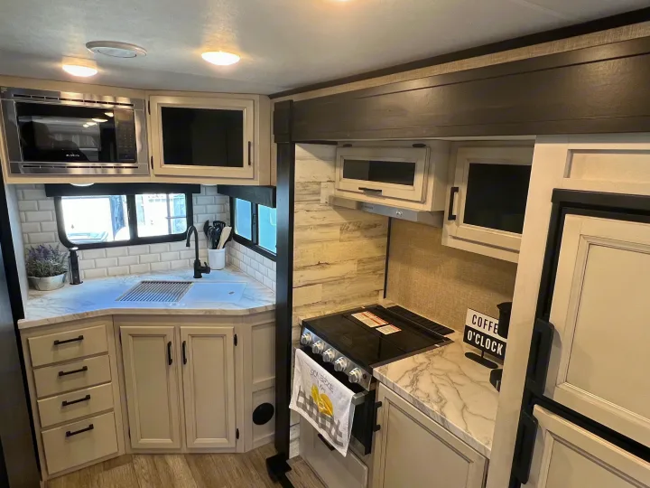 This RV rental kitchen features a microwave, stove, sink, and light-colored cabinets, providing all cooking essentials.. Jayco 21MML 2023