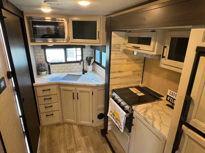 Bright, modern RV rental kitchen: microwave, sink, stove, light cabinets, subway tile backsplash & wood floors.. Jayco 21MML 2023