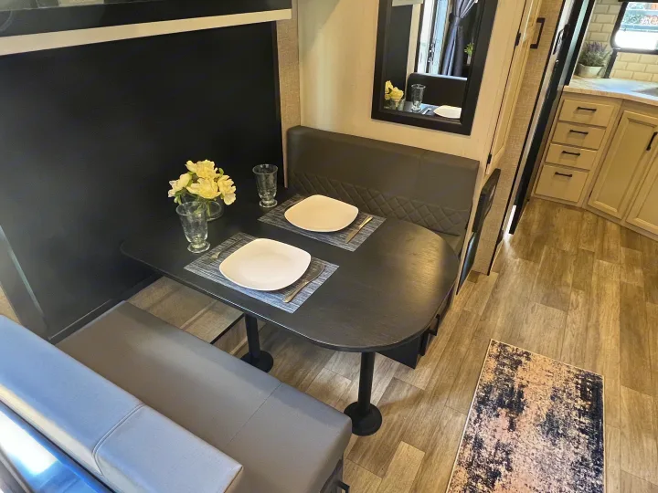 Spacious RV rental interior featuring a modern dinette with set table, bench seating, and an adjacent kitchen area.. Jayco 21MML 2023