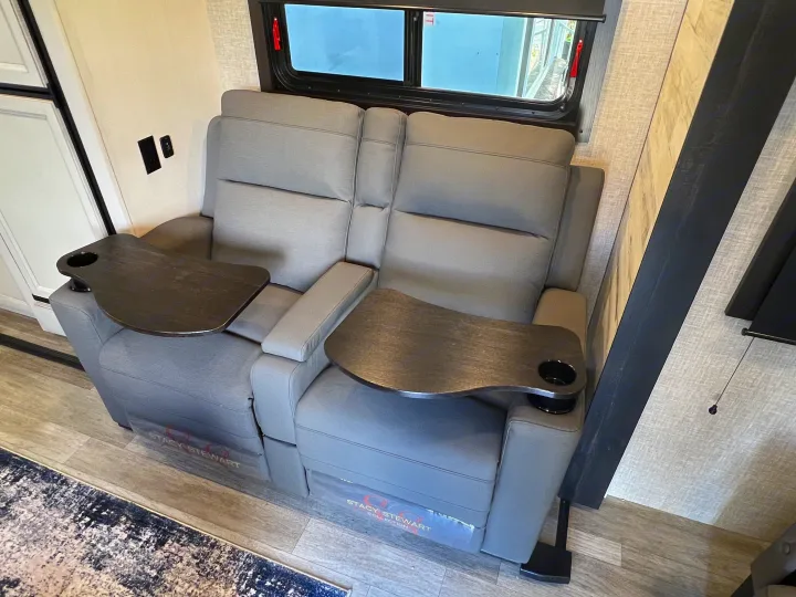 Comfortable gray recliners with swivel tables & cup holders in an RV rental interior, next to a window.. Jayco 21MML 2023