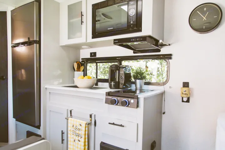 Bright, modern rv rental kitchen with stainless steel fridge, Greystone cooktop & microwave, and cheerful "Bee Happy" decor.. Forest River Salem FSX 2022