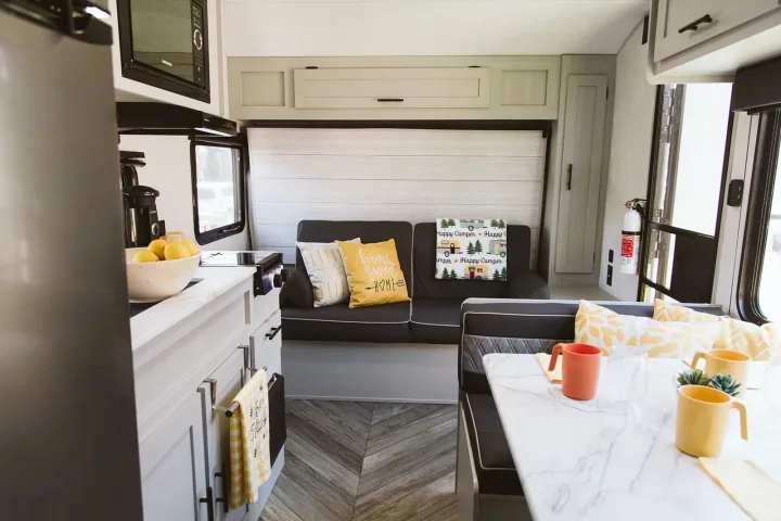 A modern RV rental interior with a bright kitchen, sofa with yellow pillows, and dining area for your next adventure.. Forest River Salem FSX 2022