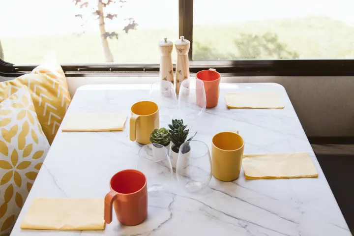 Bright RV rental interior: a dining table with yellow/orange mugs, clear glasses, and charming salt/pepper shakers.. Forest River Salem FSX 2022