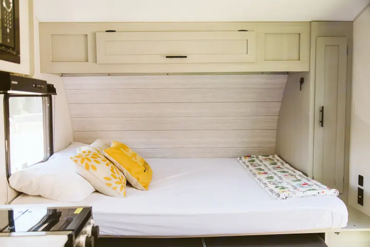 This RV rental's sleeping area features a cozy bed with white sheets, yellow pillows, and an adorable camping blanket.. Forest River Salem FSX 2022