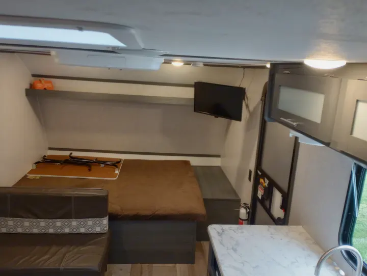 Cozy RV rental interior: bed, TV, seating, and small kitchen counter with sink, offering a compact living space.. Dutchmen 17BH 2021