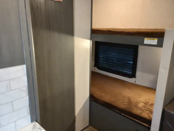 Cozy bunk beds in an RV rental, featuring a window with blinds and a tiled backsplash area.. Dutchmen 17BH 2021