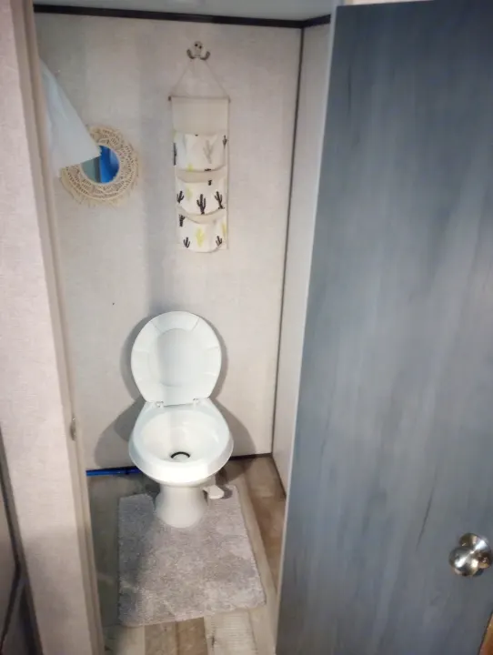 RV rental's compact bathroom shows a white toilet, gray rug, hanging cactus organizer, and decorative mirror.. Dutchmen 17BH 2021