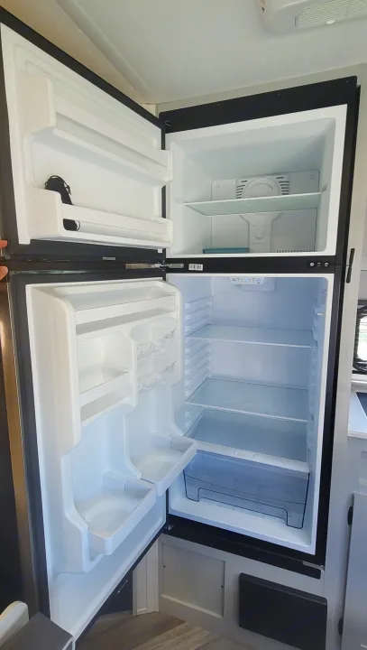 Open, empty RV rental refrigerator/freezer, showing clean shelves and storage for your journey.. Forest River Salem FSX 2022