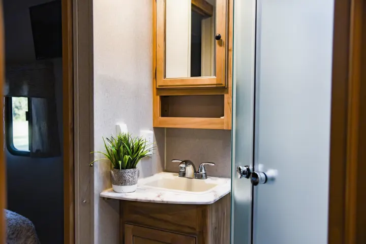 Compact RV rental bathroom with sink, vanity, mirrored cabinet, and frosted shower door.. Coachmen Freedom Express 2018