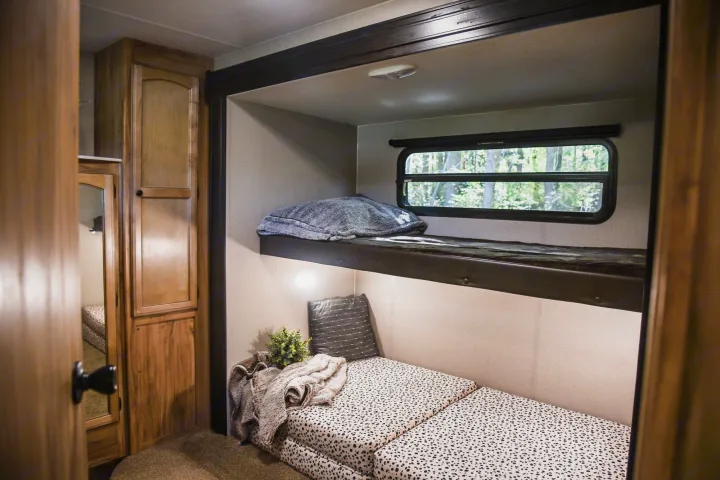 Cozy RV rental interior featuring bunk beds, a window with a forest view, and wooden cabinets for comfortable living.. Coachmen Freedom Express 2018