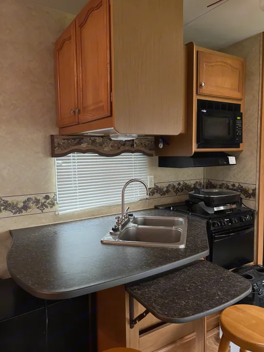 This RV rental kitchen offers wood cabinets, a double sink, microwave, stove, and a dark, speckled countertop with an extension table.. Denali Denali Fifth Wheel 2011